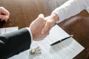 Deux mains qui se serrent au -dessous d'un contrat posé sur une table avec un stylo et des clés