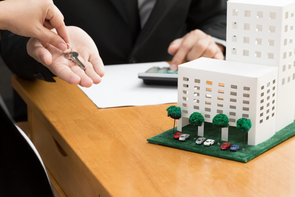 Une personne donne des clés à une autre devant une maquette d'immeuble