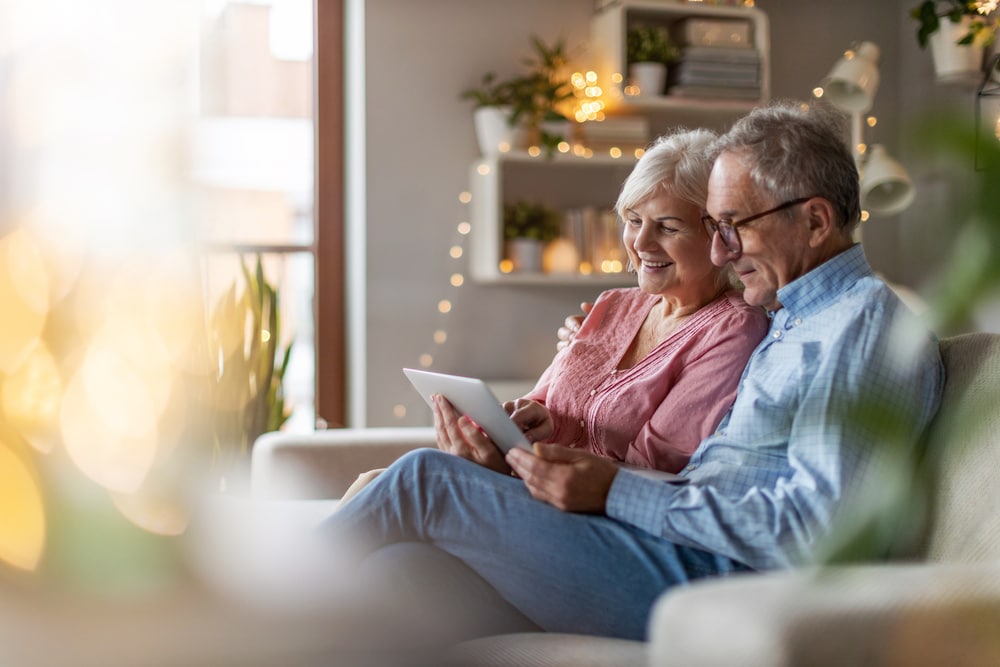 Couple de personnes âgées assis sur un canapé entrain de lire une tablette
