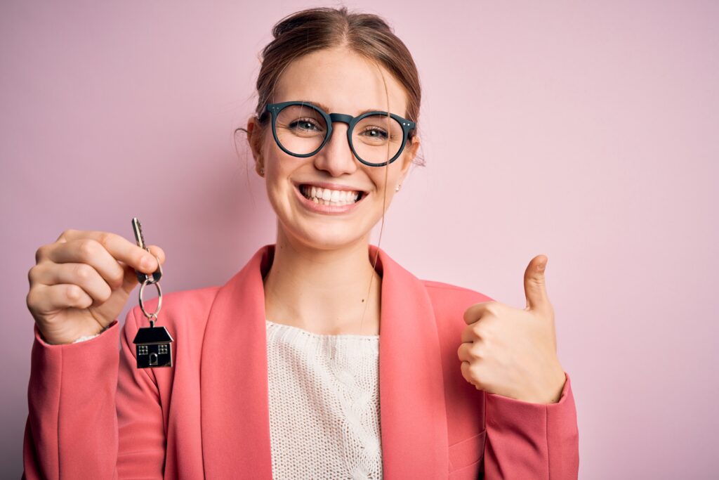 Jeune femme souriante avec un porte clé en forme de maison dans la main et le pouce en l'air